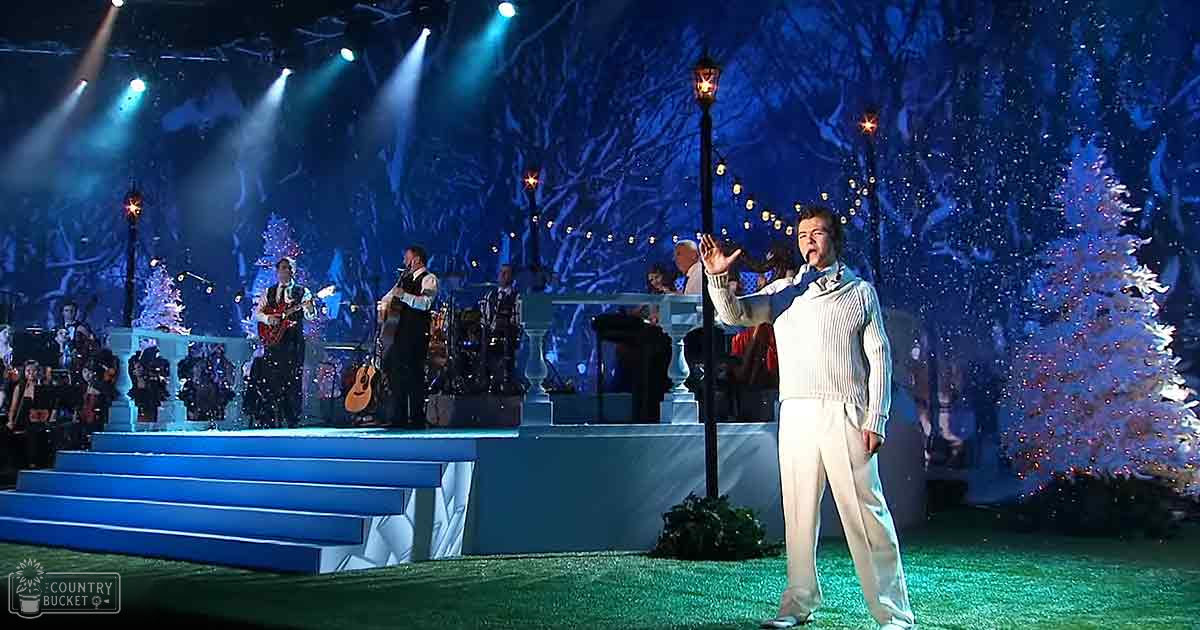 Festive outdoor performance with a performer in white attire and an orchestra under diffused daylight during the holiday season.