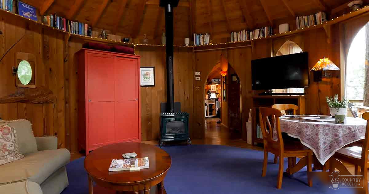 A cozy rustic interior with wooden walls, a floral-patterned sofa, red wardrobe, string lights, bookshelves filled with books and decorative items.