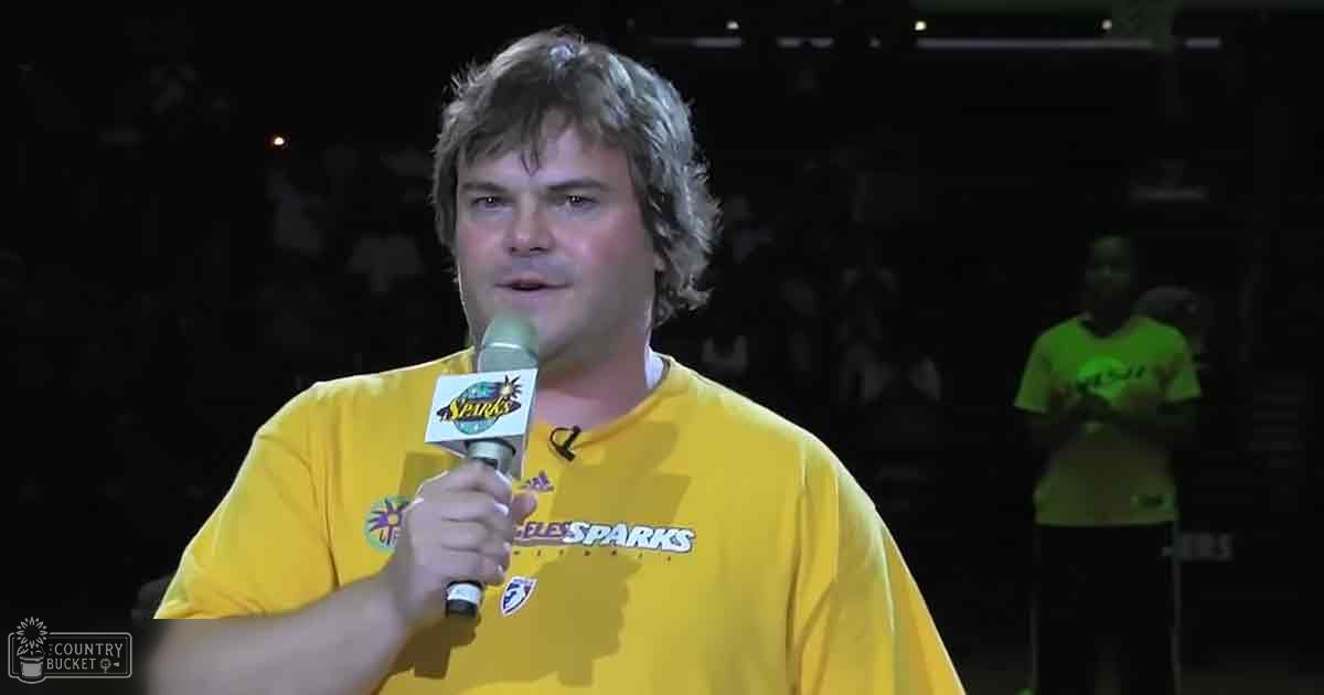 A middle-aged man wearing a yellow 'Sparks' t-shirt with a sun logo stands at an indoor sports arena; another young adult male in a neon green shirt holds a microphone behind him.