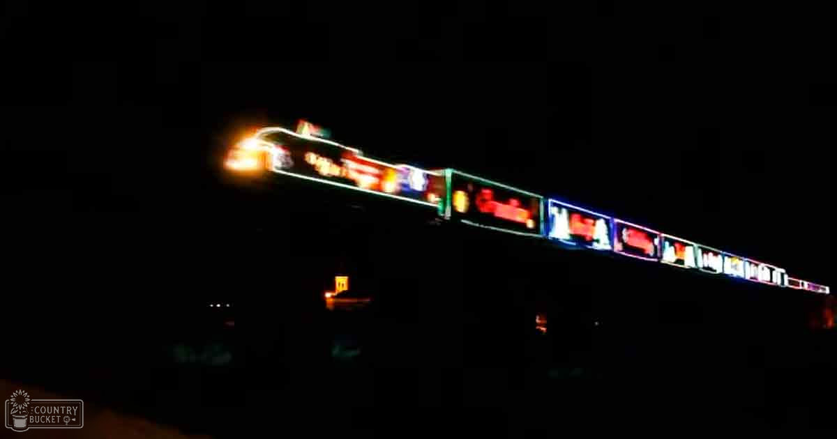 A brightly lit signboard at night with various colors and text reflecting on a wet surface below.