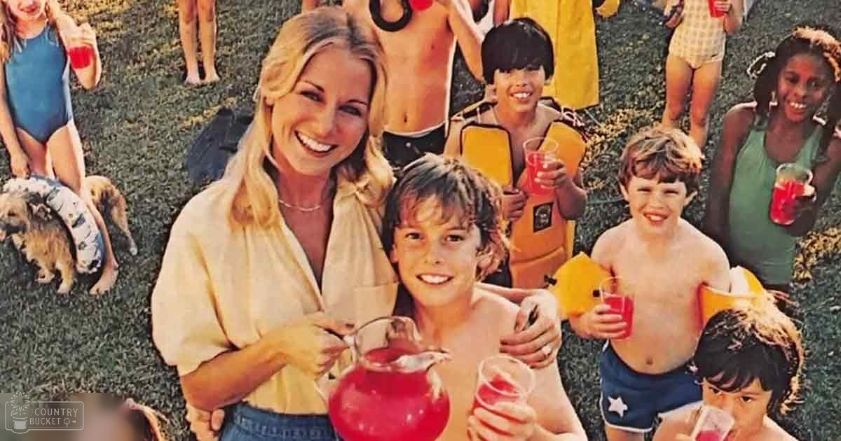 A middle-aged woman and two young children are enjoying red beverages in an outdoor setting on a warm, sunny day.