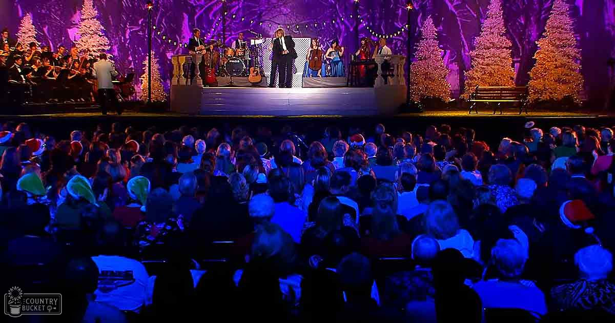 A live performance in an auditorium during Christmas season, with older adults wearing winter attire and holiday-themed headwear.
