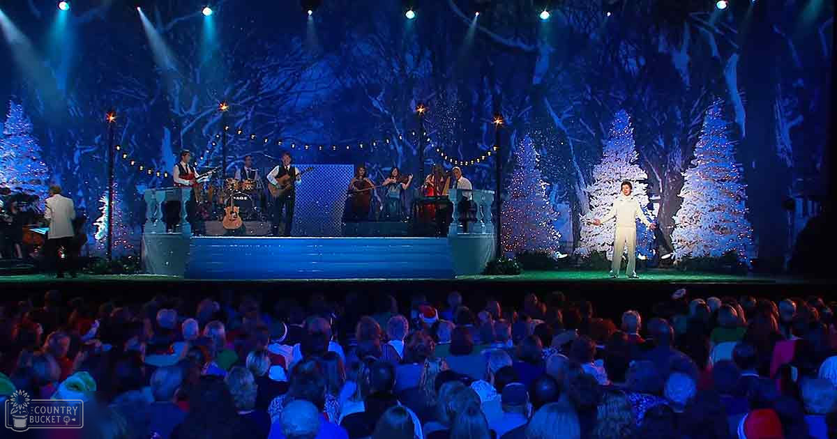 A performer singing on a snowy forest-themed stage with an audience dressed in muted winter attire.