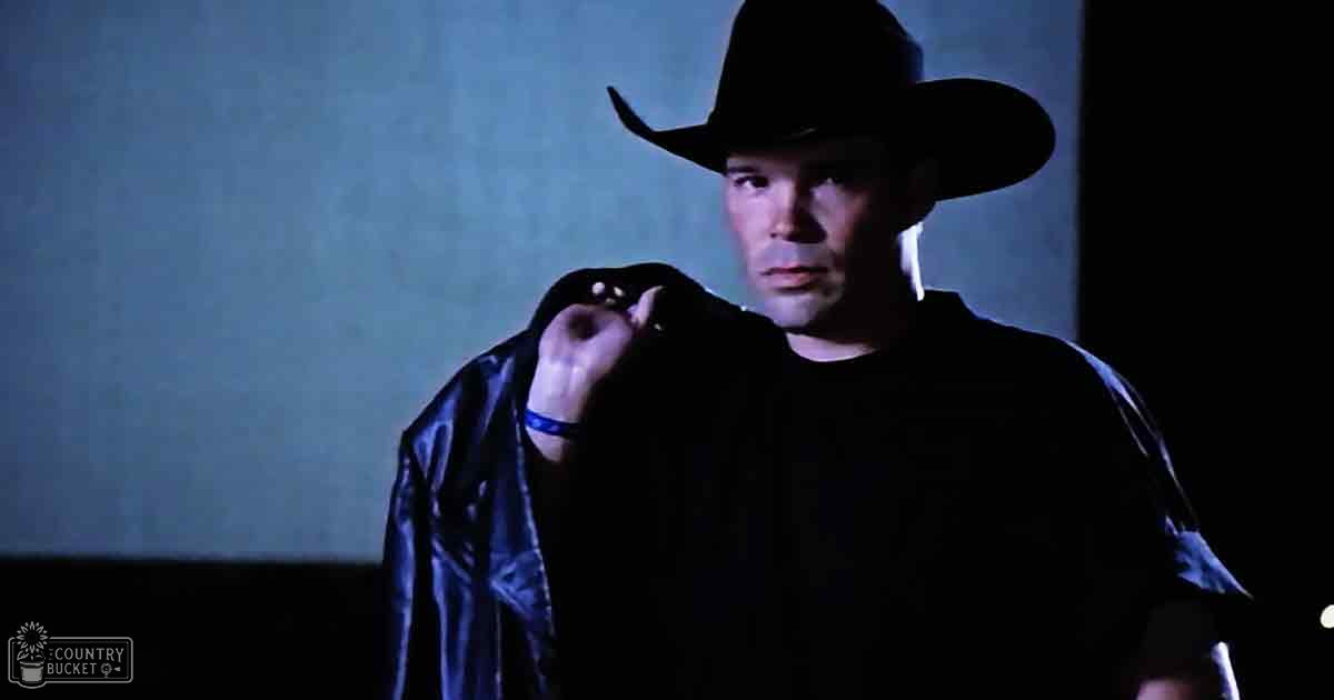 An adult male in a relaxed, modern black leather jacket and wide-brimmed hat indoors with artificial lighting.