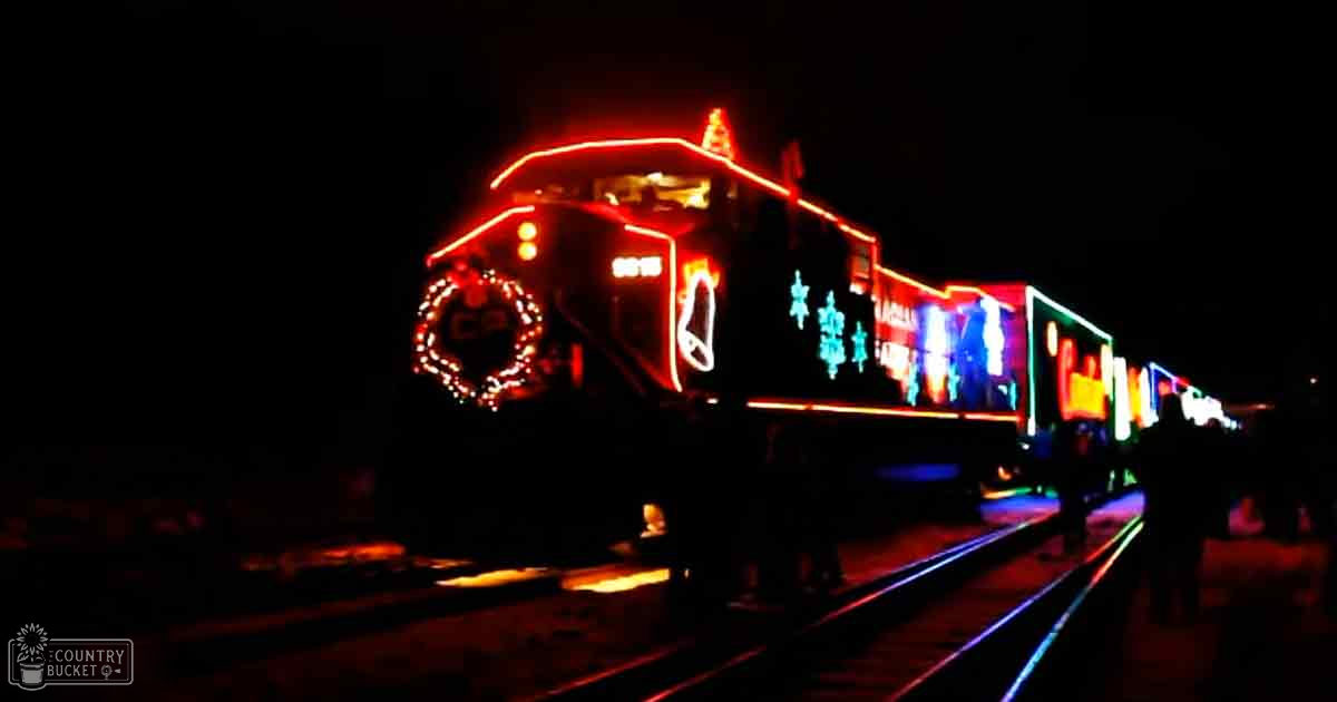 A decorated train at night adorned with bright holiday lights and festive wreaths on railway tracks during a winter celebration.