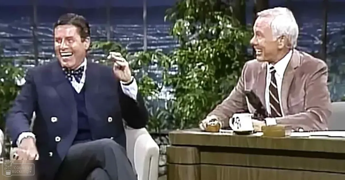 Two adult male talk show hosts in a studio setting, one wearing a dark blue suit with a patterned bow tie and the other in a light brown suit with vertical striped shirt and diagonal stripe tie.