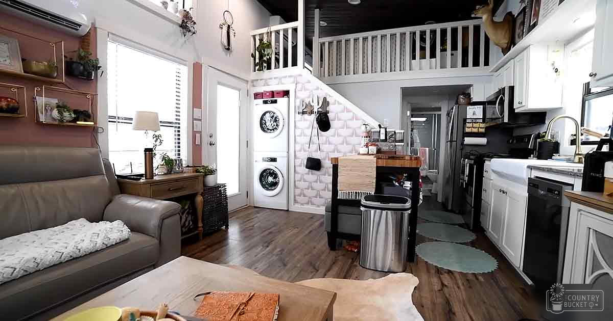 A cozy, multi-functional living space with white cabinets, brown wooden furniture, and greenery, illuminated by natural light.