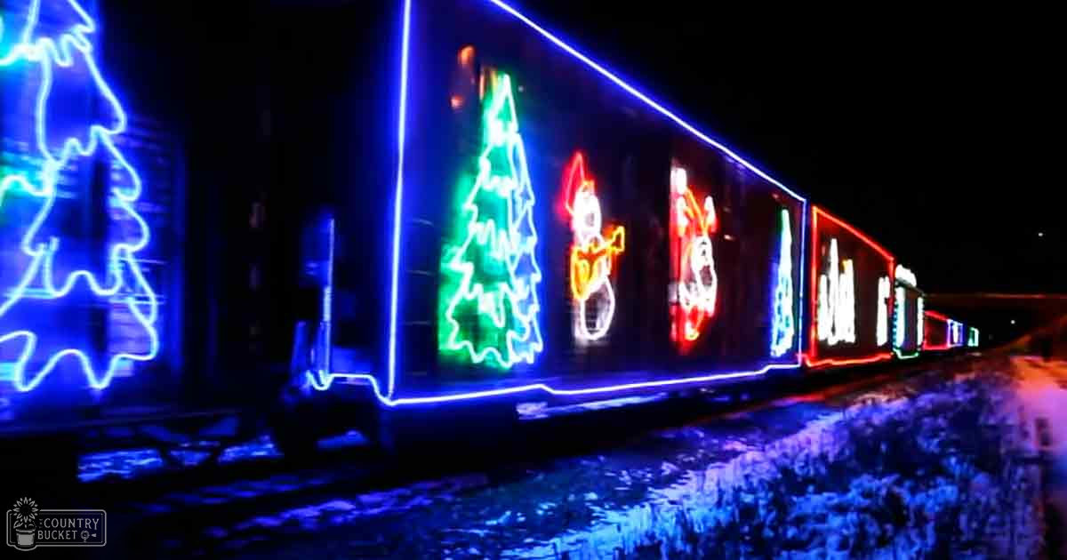 A festive outdoor winter scene with a train adorned in colorful Christmas lights against a dark, snowy backdrop.