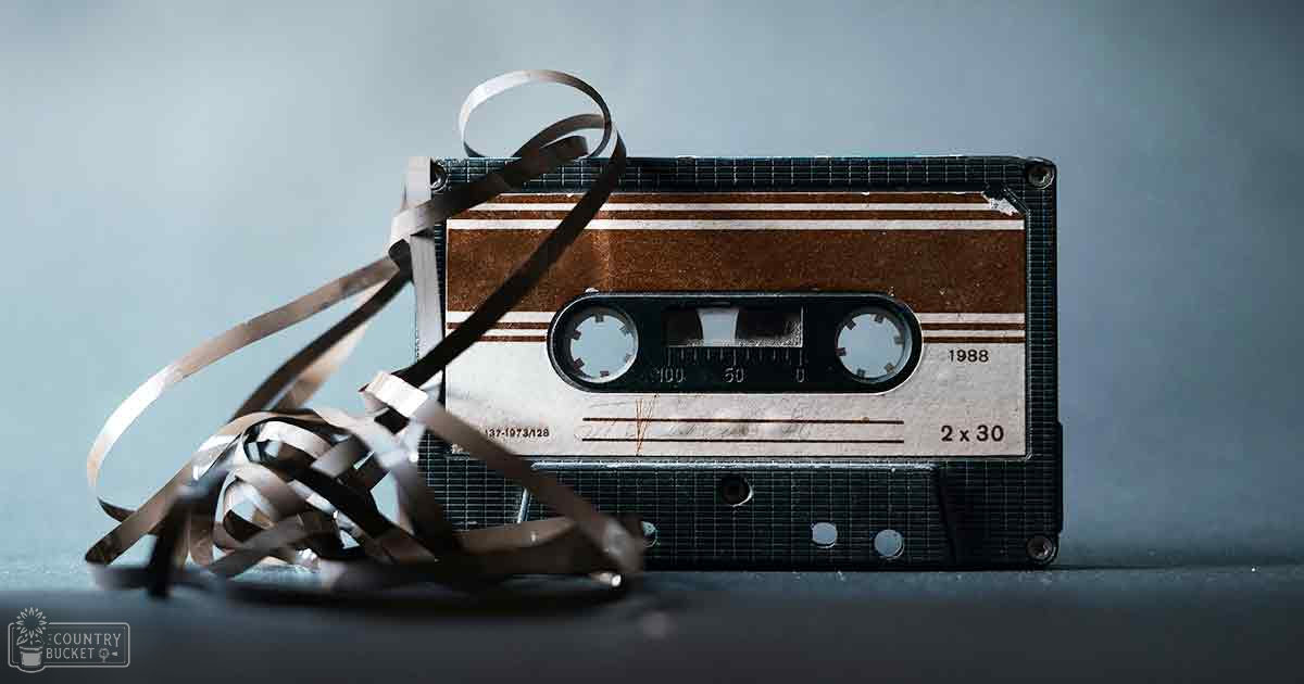 An old, worn-out vintage cassette tape with '1988' label, tangled audio tape extending from it, placed on a plain blue-gray surface.
