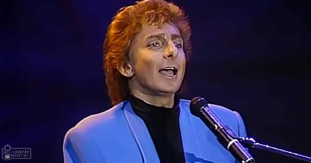 An adult male singer in a blue blazer performs at an indoor concert setting under dramatic stage lighting.