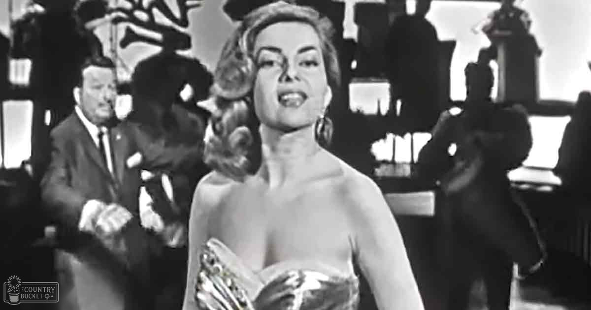 A woman in a sleeveless, strapless gown with large hoop earrings at what appears to be a formal event or performance setting; an adult male in a dark suit and white shirt with gloves on the left.