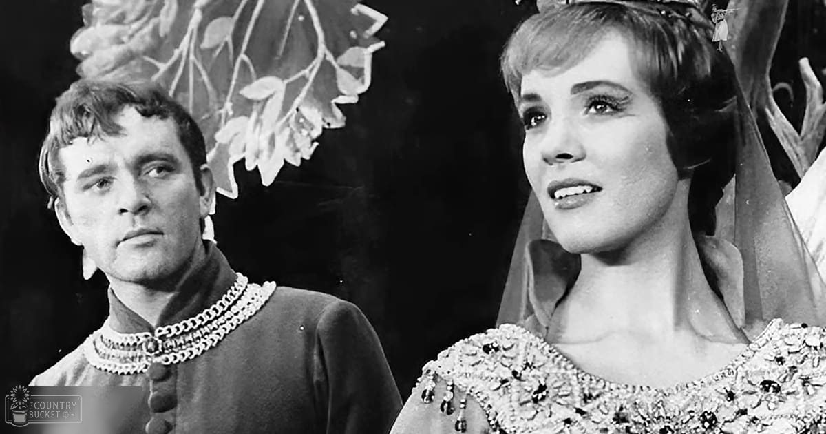 A theatrical scene with two young adults in ornate costumes on a stage set decorated with floral elements under controlled lighting, likely part of a musical or opera production.