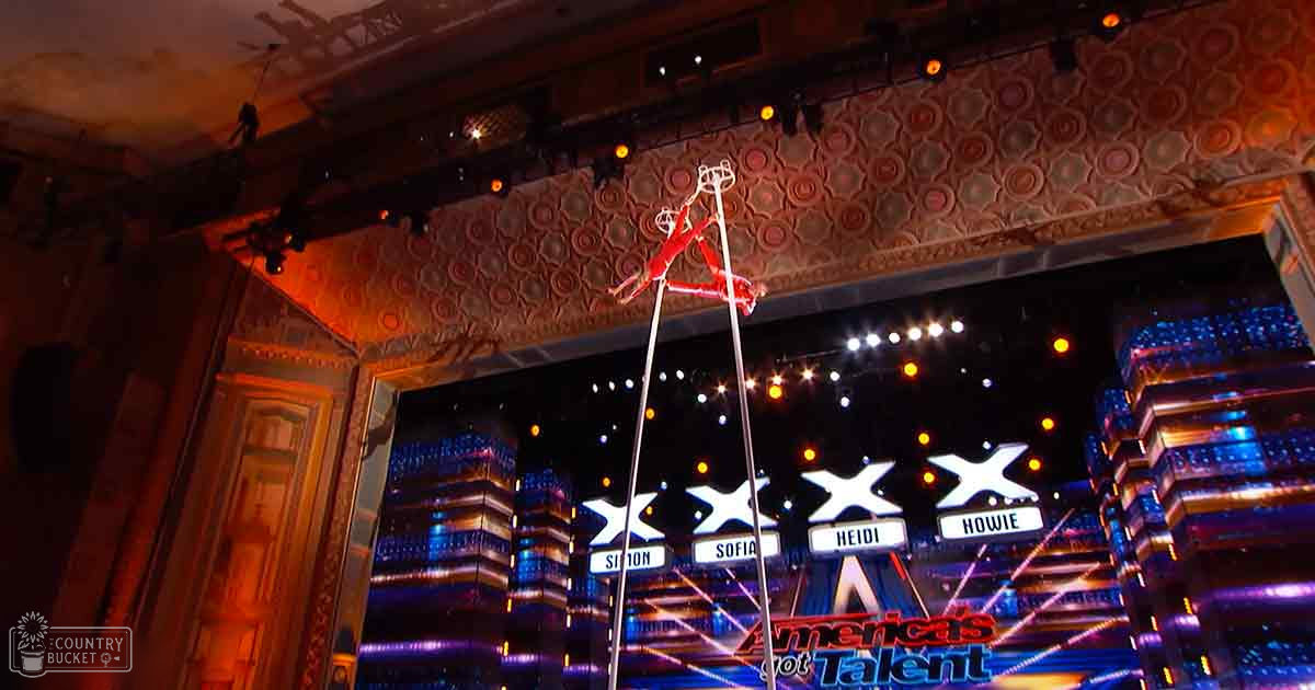 An indoor talent show stage with vibrant lights and judges' names in the background