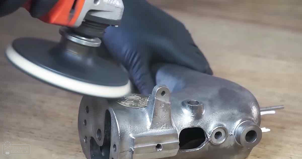 An adult male wearing dark blue latex gloves works with a red and black angle grinder on metallic parts in an indoor workshop setting.