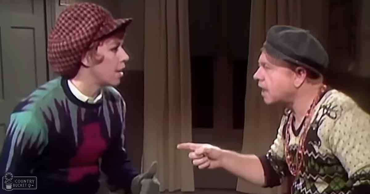 A child wearing a red and white checkered hat and a striped sweater with green, blue, red, and black stripes interacts indoors near an adult female older adult wearing a dark-colored beret-style hat and a patterned sweater. Daylight or indoor lighting illuminates the scene.