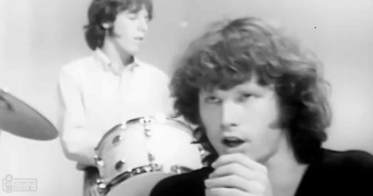 A young adult male and a teenager in casual attire playing drums against a plain backdrop under artificial light, mid-20th century.