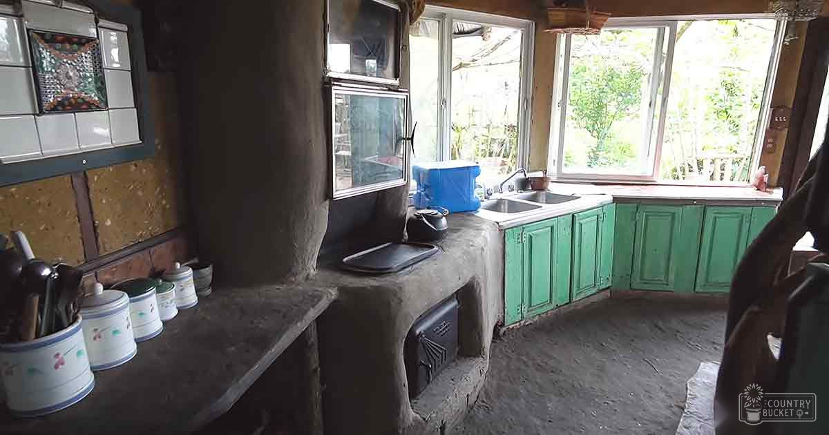 Rustic kitchen with green cabinets and concrete countertop in a natural light setting during summer or spring.
