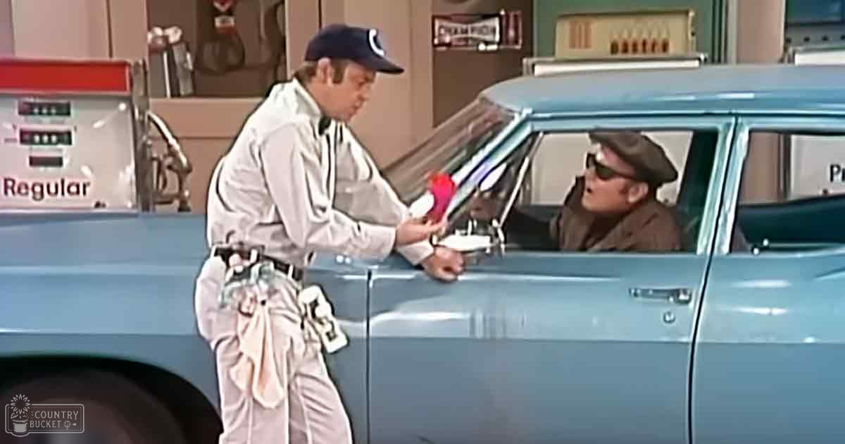 An adult male gas station attendant in a white button-down shirt, dark cap with logo, khaki pants, interacts with an older adult customer wearing a brown jacket and dark hat. Setting: Old-fashioned gas station with vintage pump labeled 'Regular', blue car from the 1950s or 60s era.