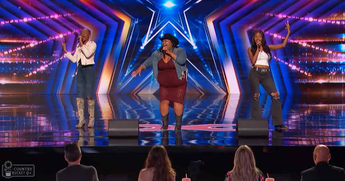 An adult male singer in a talent show performance with an audience on stage; vibrant indoor venue with geometric patterns and bright lighting.