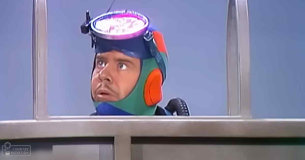 A young adult male in a futuristic space suit with blue and green accents inside a spacecraft.