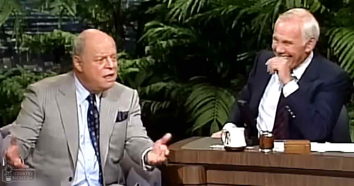 Two older adult males engaged in conversation in a talk show setting with lush green foliage backdrop, typical studio lighting.