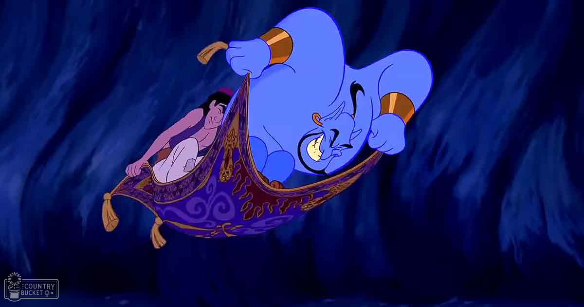 An adult male singer, Aladdin, rides a purple and gold magic carpet with Genie in a dimly lit cave-like setting.