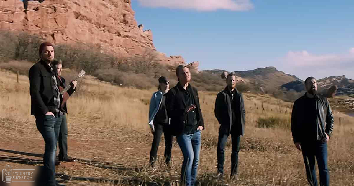 A group of musicians in an outdoor setting with a rocky hillside background, likely autumn or winter.