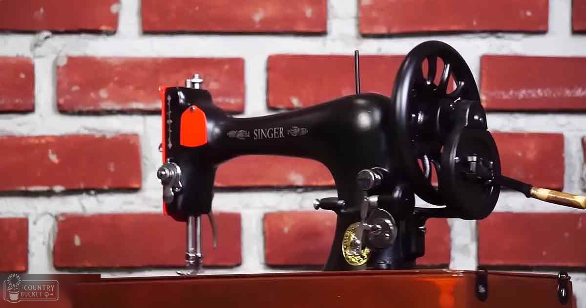 Vintage Singer sewing machine with a red and black color scheme, placed against a brick wall with a brown leather strap or belt in front.