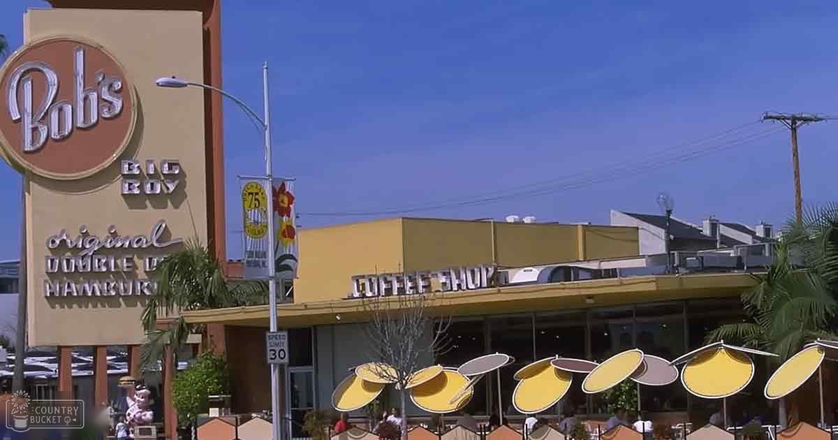 Bright sunny day at Bob's Big Boy Restaurant with yellow umbrellas, clear blue skies, and palm trees in an outdoor seating area.