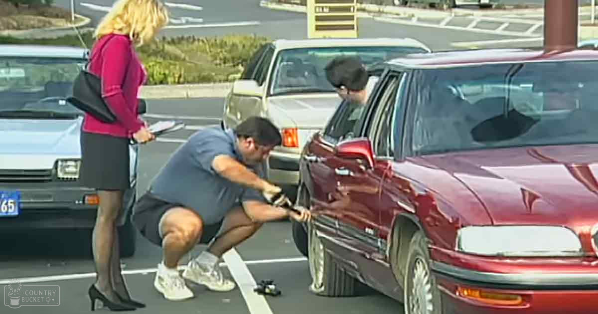 A young adult male works on a maroon sedan in what appears to be a parking lot with multiple vehicles and tools visible. An adult female, wearing purple and black, holds a clipboard or notepad nearby.
