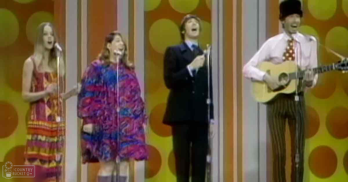 A musical performance scene with performers in colorful outfits against a vibrant backdrop with vertical stripes and circular patterns.