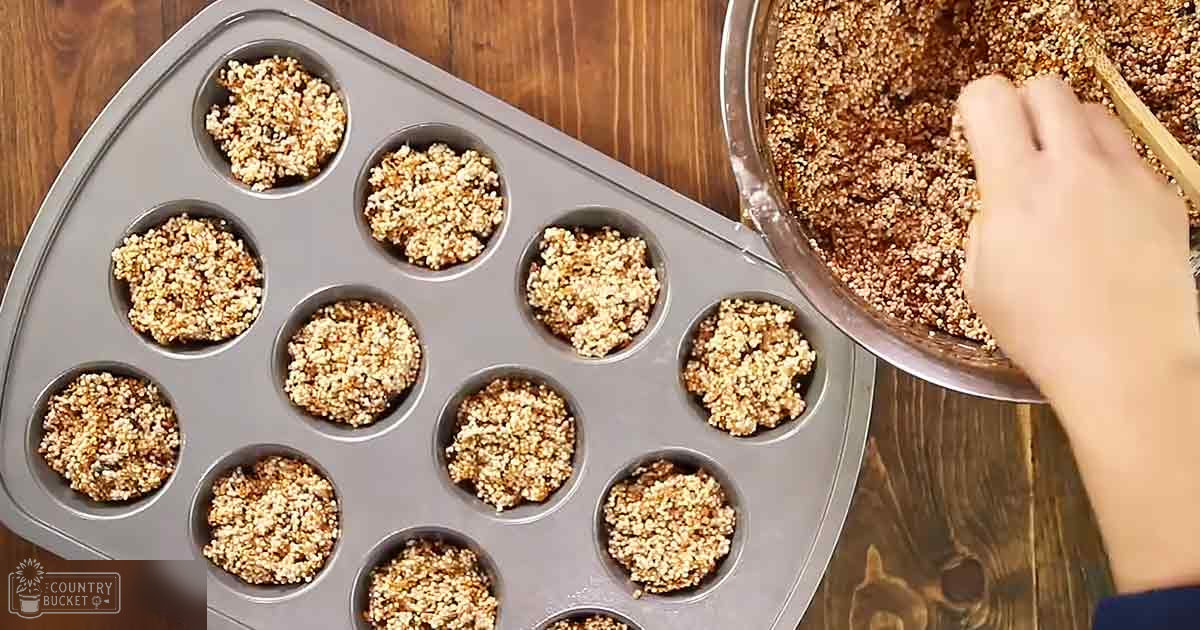 Adult female baking muffins in a kitchen with natural light, wooden table and countertop, crumbly mixture being filled into tins.