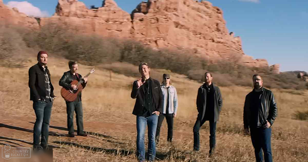 Adult males in a desert-like setting with red rock formations, playing music on an open field during late autumn or early spring daytime with natural sunlight.