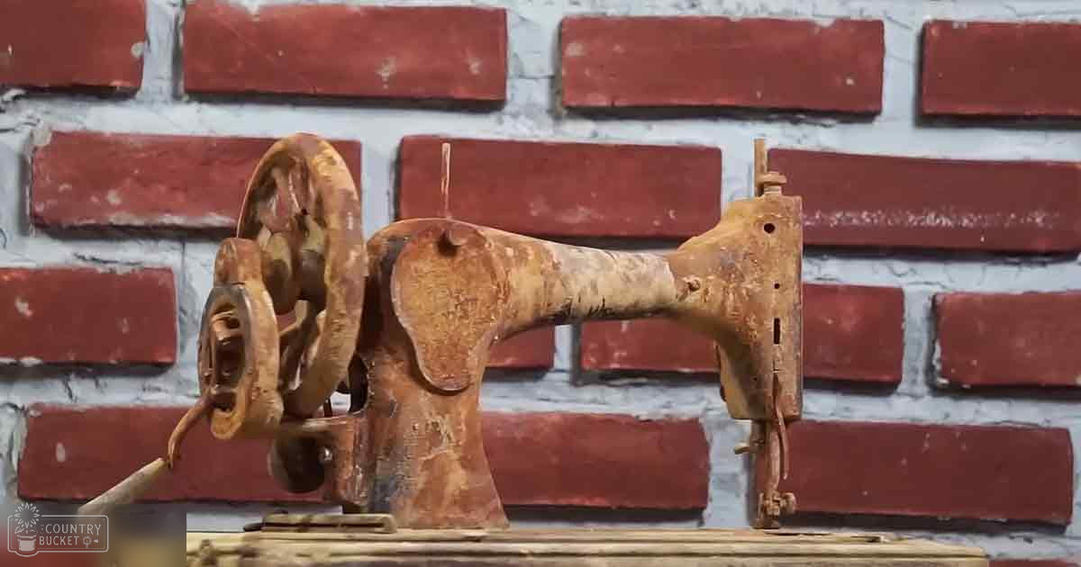 A vintage sewing machine with a worn appearance, set against a red-brick wall backdrop in an indoor setting.