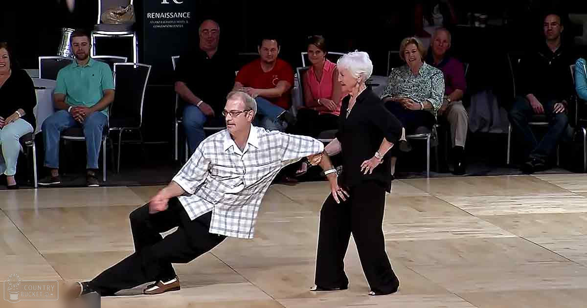A ballroom dance performance with an adult male in a white and gray checkered shirt, middle-aged adults seated as spectators, and a sign for Renaissance Atlanta Waterfront Hotel & Convention Center visible in the background.