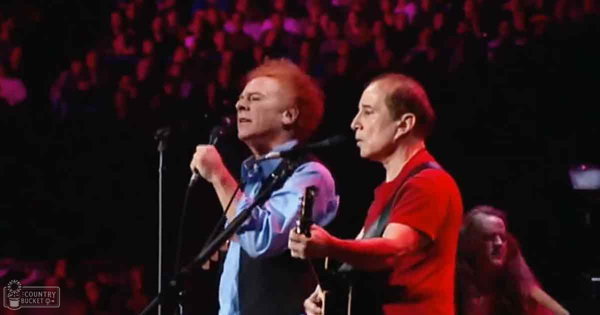 Adult male performers wearing casual attire on a brightly lit indoor concert stage with an engaged crowd in the background.