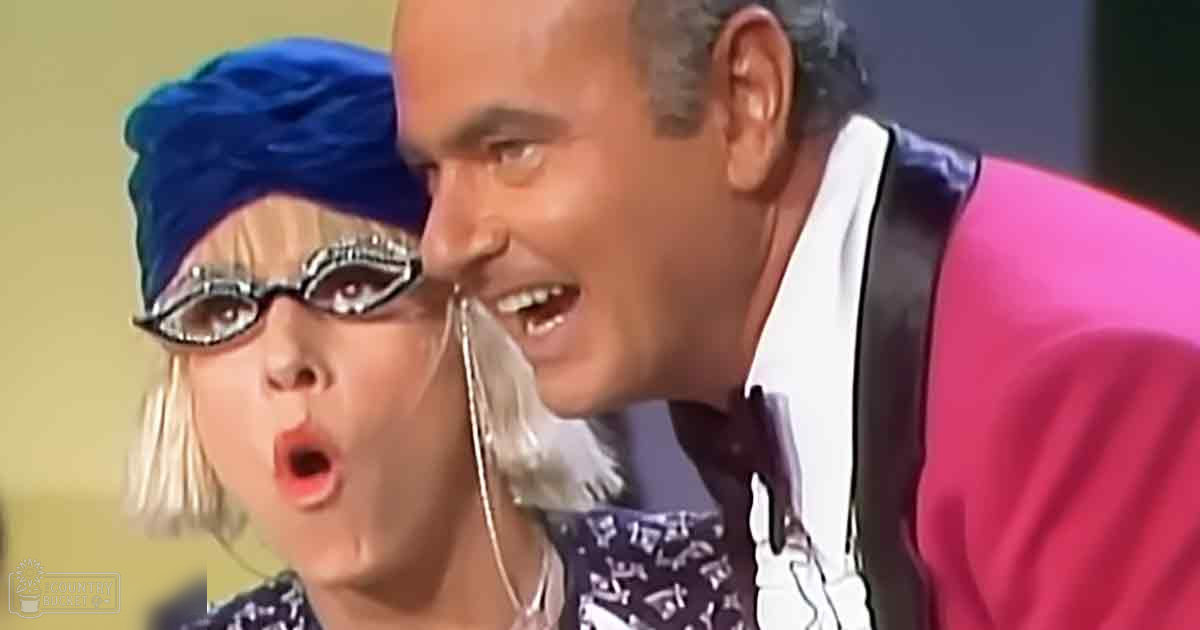 A comedic scene from a TV show or film set in an indoor studio environment with two characters, one child female wearing a blue headscarf and oversized black sunglasses, and an adult male in a pink jacket over a white shirt.