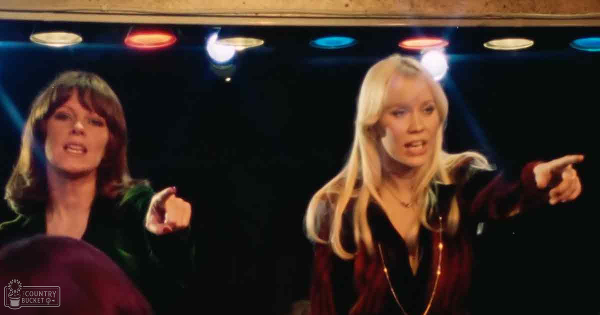 Two women in a stage setting with dark red and green jackets, surrounded by professional stage lighting.