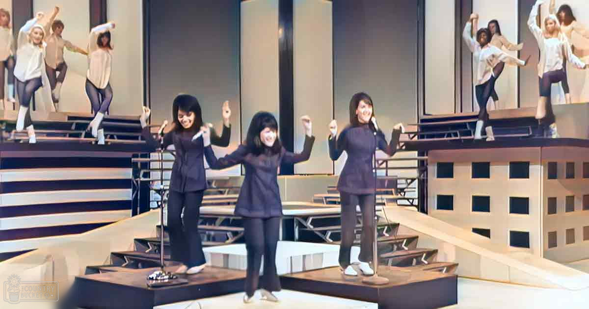 A theatrical performance in an indoor theater with bright stage lighting, with young adult females dressed in dark blue outfits and white shoes.