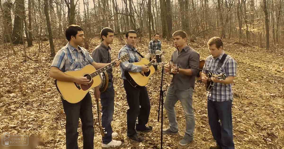 Young adults performing music outdoors in a wooded area with bare trees and fallen leaves on the ground.