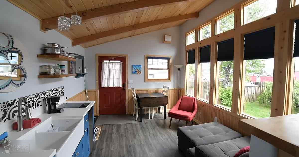 A cozy indoor space with light blue walls, wooden furniture, and large windows overlooking greenery.