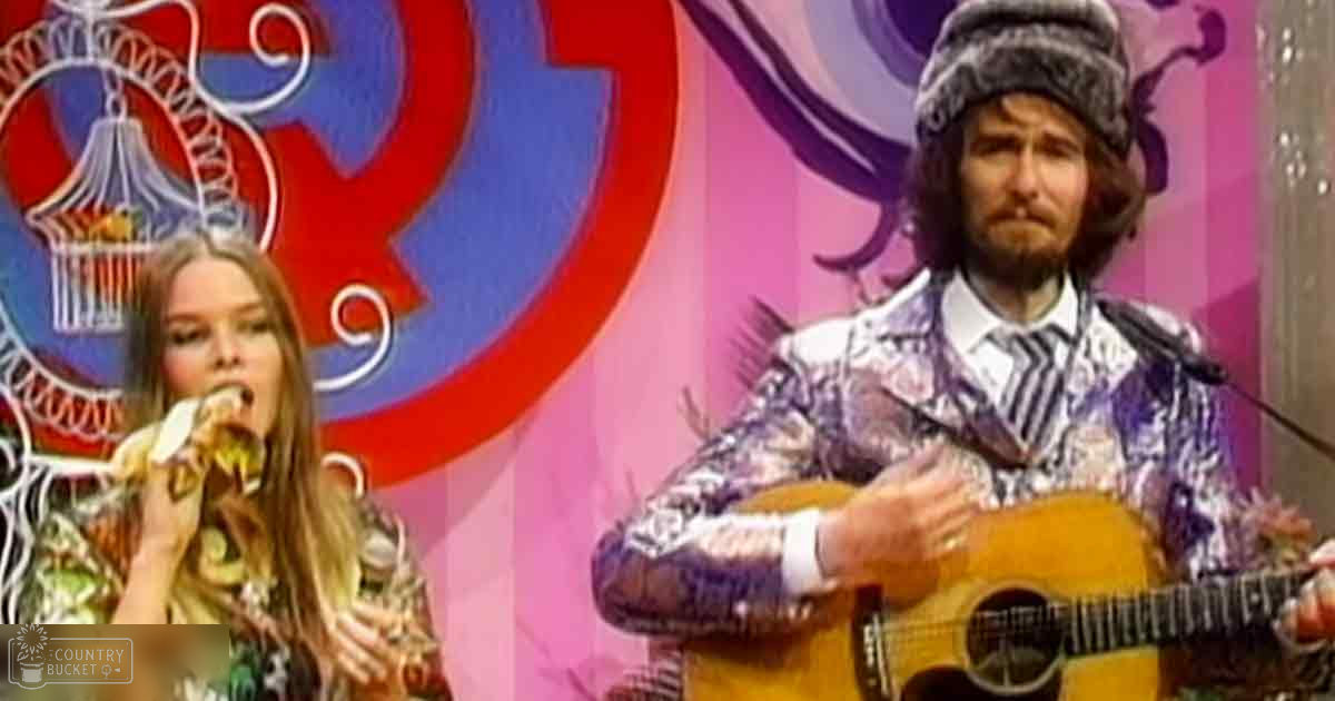A musical performance scene with a young adult female wearing a floral dress and an adult male in a patterned suit jacket, holding microphones against a vibrant abstract background.
