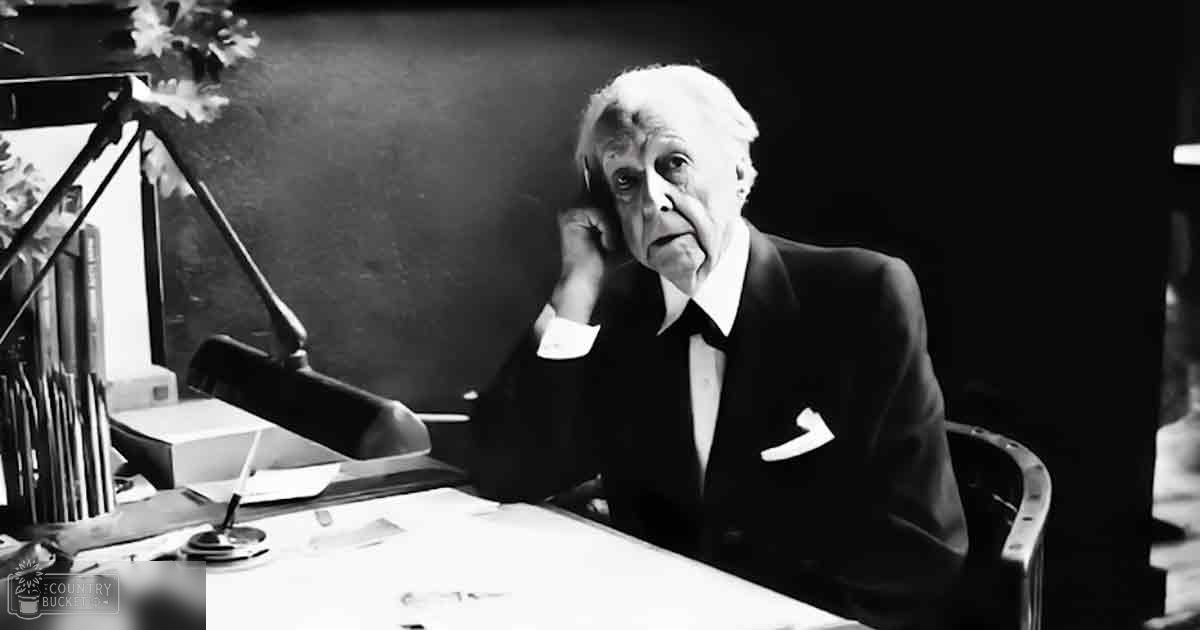 An older adult male wearing a formal suit in an office or study setting, with a desk with a lamp and flower arrangement under indoor lighting.