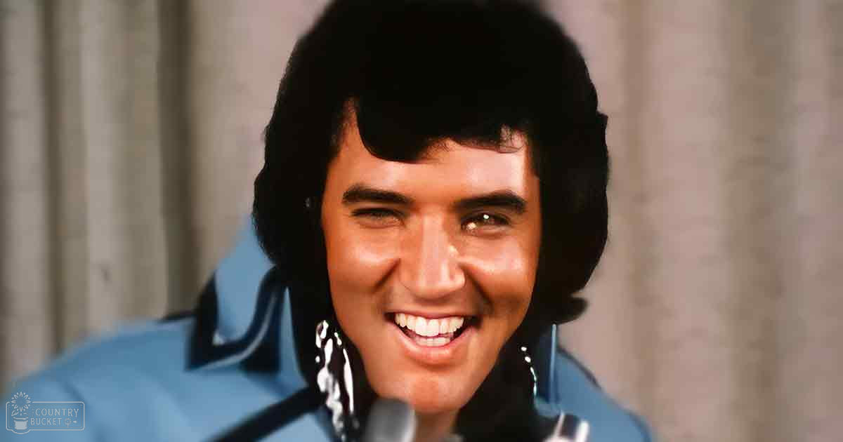 A young adult male in a tailored blue jacket with black trim stands indoors, neutral-colored curtains in the background suggest daylight.