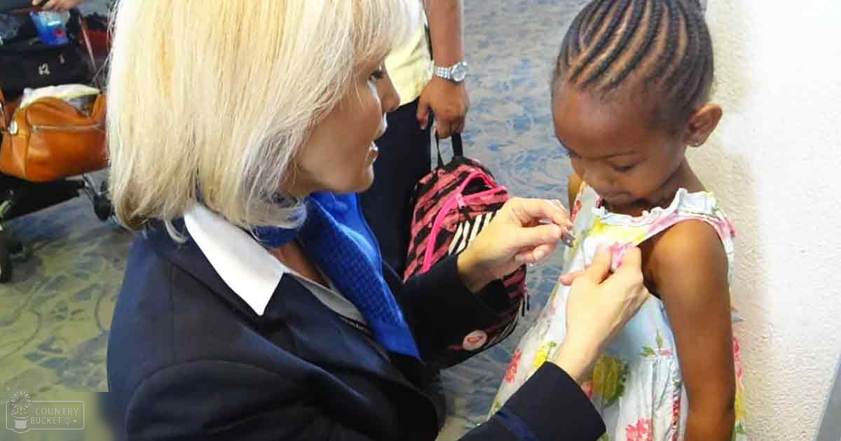 Healthcare professional administering an injection to a young child in an airport setting, with natural daylight and patterned carpet visible.
