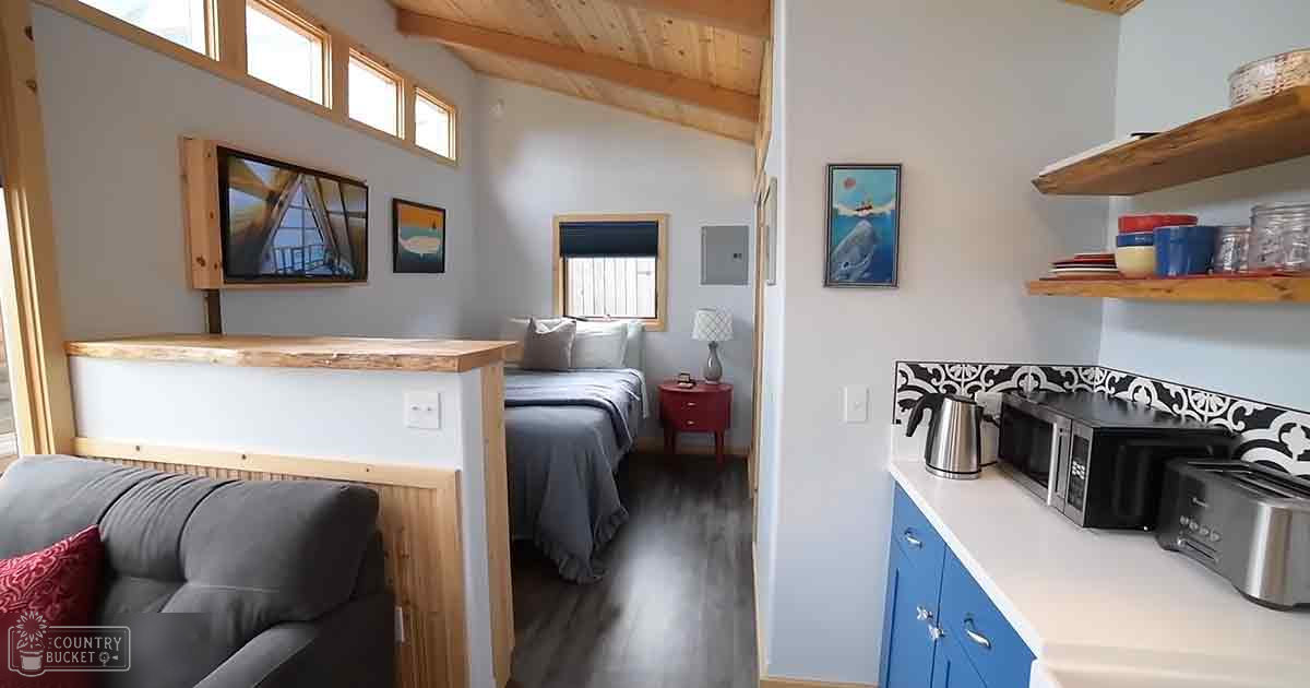 Compact living space with a bed, kitchenette, and wooden partition in an indoor setting with natural light.