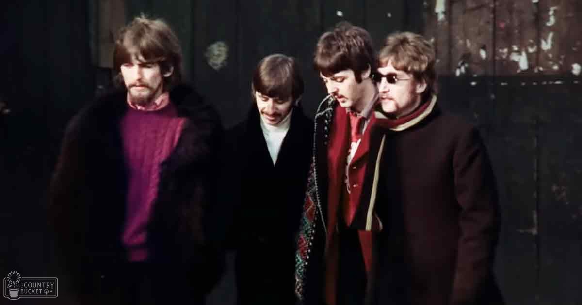 Four young adult males wearing dark coats with fur-lined hoods and various colored shirts in an urban setting with a worn wall or door in the background.