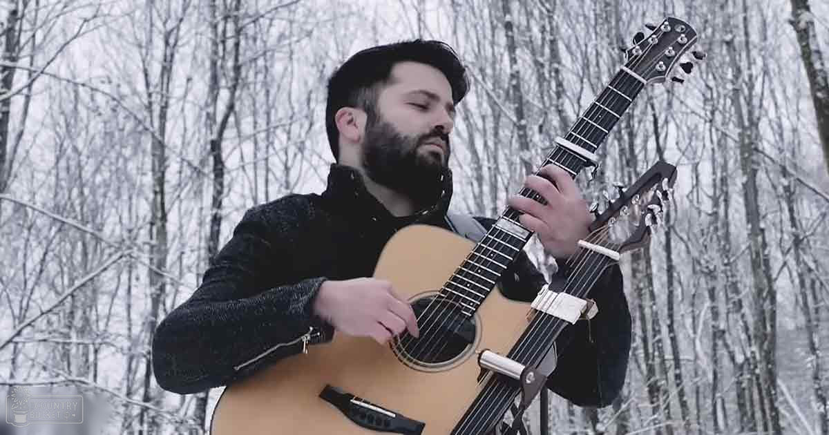 A man in a dark jacket plays guitar amidst a snowy forest during winter.