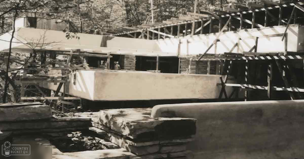 A shipyard with a partially constructed wooden boat under construction amidst trees and scaffolding at daytime in muted black-and-white tones.