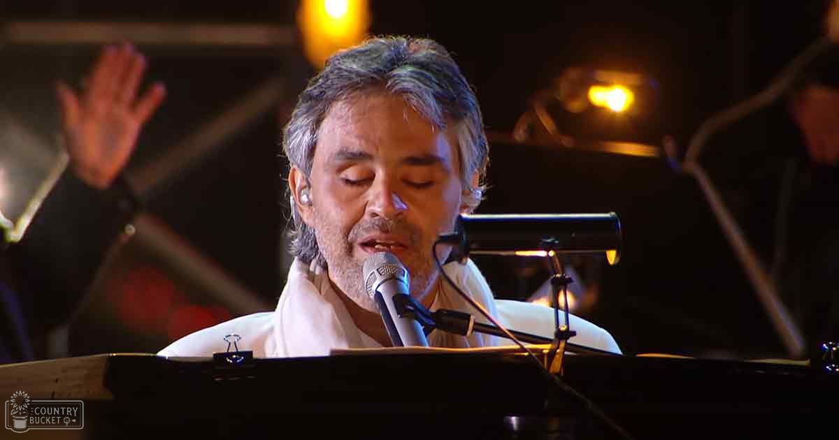 A middle-aged man performing at an indoor concert setting, wearing a white shirt and surrounded by microphones and stage lighting.